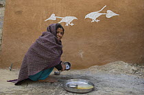 Rajasthani woman beside traditional painting on mud wall of house during Diwali festival, Bada Gaire Killa village, Rajasthan India