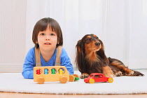 Portrait of young boy playing with toys, and long haired Dachshund