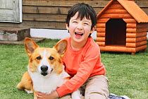 Portrait of young boy with Welsh Corgi, in the garden, with kennel behind