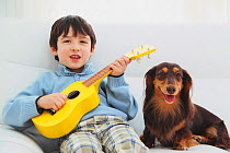 Portrait of young boy sitting and playing toy guitar with Longhaired Dachshund