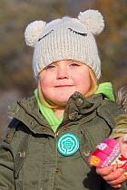 Young girl wearing a badge for The National Forest, with the volunteers planting sapling trees as part of The National Forest's planting day, Moira, Derbyshire, UK, November 2010
