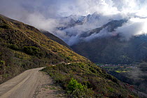 Unpaved road with the village of Totoral and Illimani Mountain partially obscured by clouds in the distance, Bolivia, October 2013.