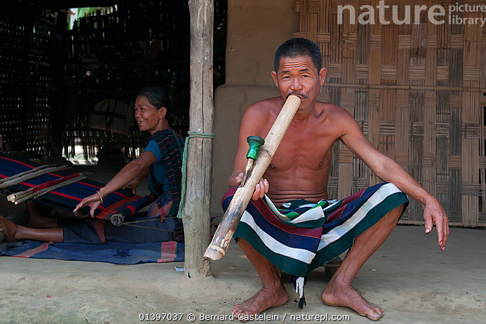 Stock photo of Man of Chakma tribe, smoking a bamboo pipe (daba), with  woman weaving on…. Available for sale on
