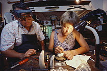 Young woman working on scrimshaw while proprietor of store oversees, Maui, Hawaii