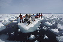 Inuit guide and film crew ferrying supplies and snowmobiles on icefloe, Arctic