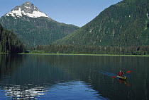 Kayaker paddling in calm seas along mountainous coast of southeast Alaska
