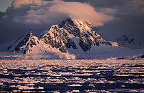 Snow-covered mountain range with icebergs falling into ocean and ice floes at Gerlache Strait, Antarctic Peninsula, Antarctica