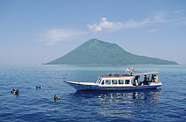 Nusantara Dive Center boat anchored at Bunaken Island dive site with Manado Tua Volcano in the distance, Manado, North Sulawesi, Indonesia