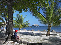 Tourist resting under palm trees on beach at Palmetto Bay, Roatan Island, Honduras
