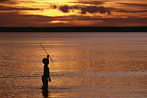 Young boy spear fishing at sunset in the mouth of the Kikori River Delta, Papua New Guinea
