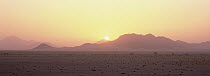 Sun setting behind mountains and dunes on eastern border, Namib-Naukluft National Park, Namibia