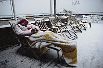 Dedicated Antarctic tourist asleep on deckchair during snowfall, Amundsen Sea, Antarctica