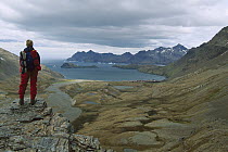 Tourist standing on the Fortuna Saddle views the derelict Norwegian Stromness whaling station, South Georgia Island