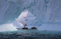 Tourists cruise in inflatable boats, close to large iceberg arch, Enterprise Island, Antarctica Peninsula, Antarctica