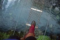 Hiker crossing wire bridge, Tuke River, New Zealand