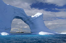 Sailboat seen through sea arch in iceberg, Gerlache Strait, Antarctica