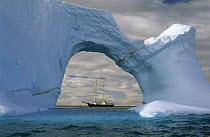 Sailboat seen through sea arch in iceberg, Gerlache Strait, Antarctica