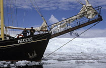 Two tourists relaxing on the deck of sailboat Meander as it navigates through bergy bits, Lemaire Channel, Antarctica