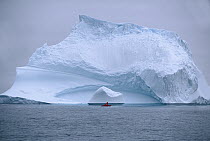 Red rubber boat with two expedition members circle floating iceberg, summer season, Labrador Sea, Labrador, Canada