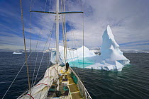 Sailboat near iceberg with shallow pool created by pounding waves and melting process accelerated by global warming, Antarctica