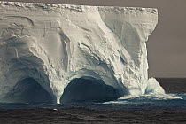 Wave crashing into eroded tunnel of tabular iceberg, Antarctica