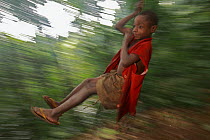 Baka child swinging on rope made from a single piece of bark, Cameroon