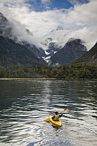 Tourist in kayak exploring Harrison Cove with Mount Pembroke above, Milford Sound, Fiordland National Park, New Zealand