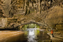 Moria Gate Arch with limestone stalagtites on roof and tourist watching swollen Oparara River, Kahurangi National Park, near Karamea, New Zealand