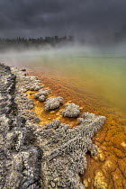 Champagne Pool as burst of sunshine lights up foreshore during day with blowing mist and heavy rain, Waiotapu Thermal Wonderland, Rotorua, New Zealand