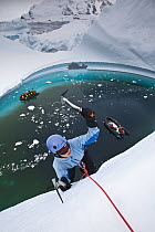 Woman climber ice climbing on grounded iceberg with cruise ship passengers looking on, Pleneau Island, Antarctic Peninsula, Antarctica