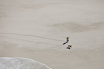 Fisherman and dog walking on beach, Cape Agulhas, South Africa