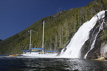 Sail boat driving up to at base of waterfall in Kynoch Inlet, British Columbia, Canada