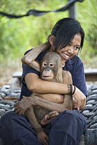 Orangutan (Pongo pygmaeus) caretaker holding juvenile, Orangutan Care Center, Borneo, Indonesia
