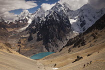 Trekkers descend steep scree slopes from Santa Rosa Pass with Jurau Lake and peaks of Yerupaja and Siula Grande in clouds, Cordillera Huayhuash, Andes, Peru
