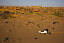 Photographer's car on sand dunes with paraglider shadow near Walvis Bay, Namib Desert, Namibia