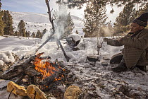 Tsataan man making tea in taiga forest while bread cooks beside the open fire during spring Reindeer round up, Mongolia