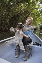Brown-throated Three-toed Sloth (Bradypus variegatus) biologist, Rebecca Cliffe, holding sloth wearing sloth backpack while traveling in boat to release site, Aviarios Sloth Sanctuary, Costa Rica