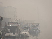 Boats in dense haze caused by fire, set by humans to clear rainforest, Kumai River, Kumai, Central Kalimantan, Borneo, Indonesia. October, 2015