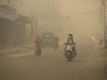 Motorcycles on road in dense haze caused by fire, set by humans to clear rainforest, Kumai, Central Kalimantan, Borneo, Indonesia. October, 2015