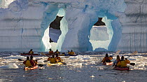 Kayakers approaching arches in iceberg, Cierva Cove, Antarctic Peninsula, Antarctica