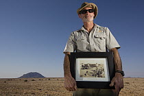 Namib Desert Horse (Equus caballus) conservationist, Piet Swieger, holding historical photograph of horses in the desert, Namib-Naukluft National Park, Namibia