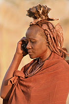 Married Himba woman talking on cell phone, Kaokoveld Desert, Namibia