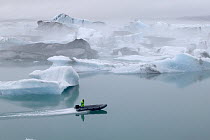 Boater, in an inflatable boat, speeding by icebergs from Vatnajokull Glacier, Jokalsarlon Lagoon, Iceland