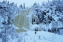 Photographer climbing up to frozen waterfall, Finland