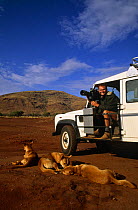 Simon King on location to film dingos; sitting in Land Rover with film camera, dingos sleeping nearby, Australia, 1995