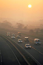 Sun shining through the mist over motorway traffic on M5. Avon, UK, November 1995.