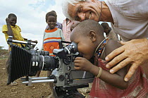 Masai child looking through film camera lens with cameraman Alan Hayward, on location for BBC series Lifesense, Kenya, East Africa 1991