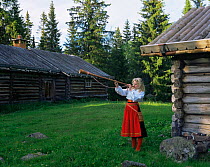 Girl playing musical instrument in traditional clothing, outside traditional wooden chalets, Dalarna, Sweden