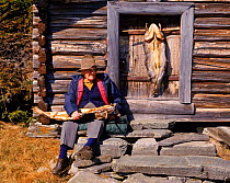 Old fisherman with  pike by log cabin. Norway