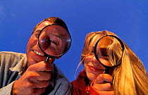 Man and woman examining plants using magnifying glass - field botany studies